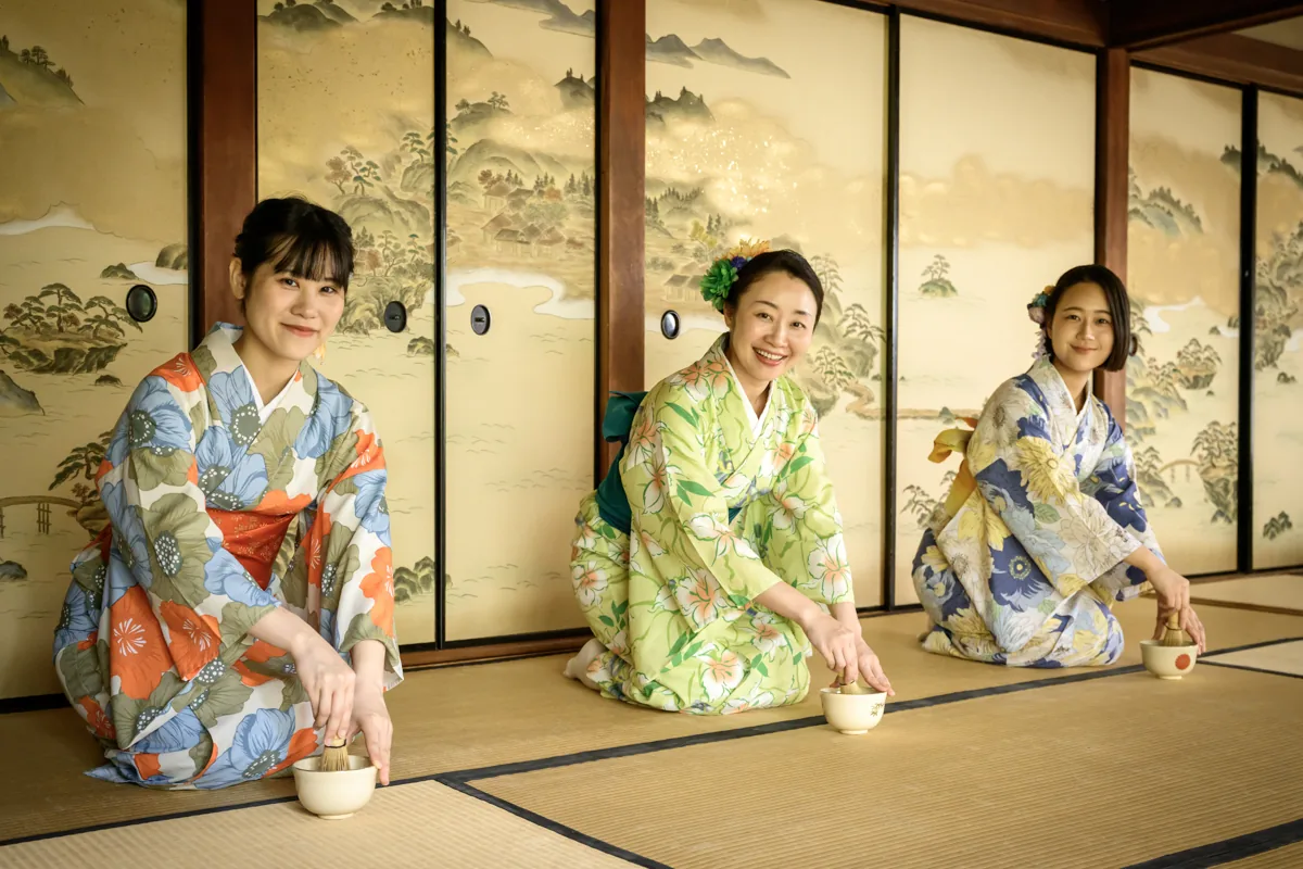 Three guests in colorful kimono whisking matcha in a Kyoto tea room